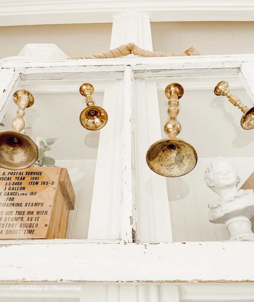 Vintage brass candlesticks hanging from white salvaged window on bookcase.