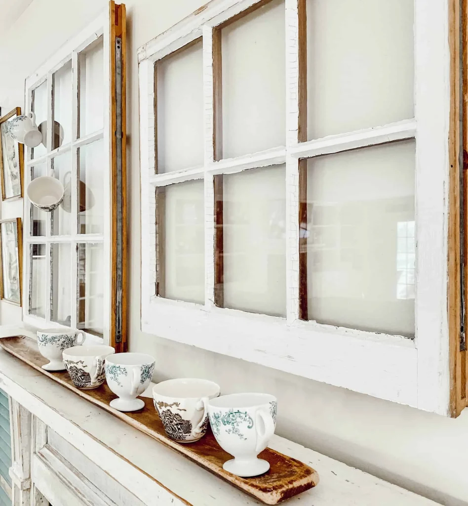 Salvaged windows on wall with row of vintage teacups on mantel.