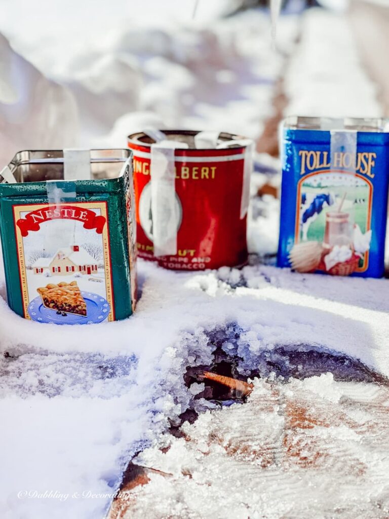 Three tin cans in snow freezing DIY candles for winter diy project.