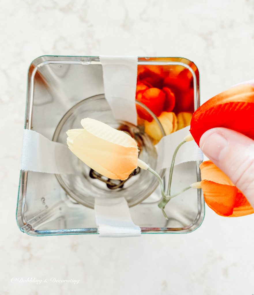 Faux tulips in hand being placed into a tin as part of a DIY frozen candle tutorial.