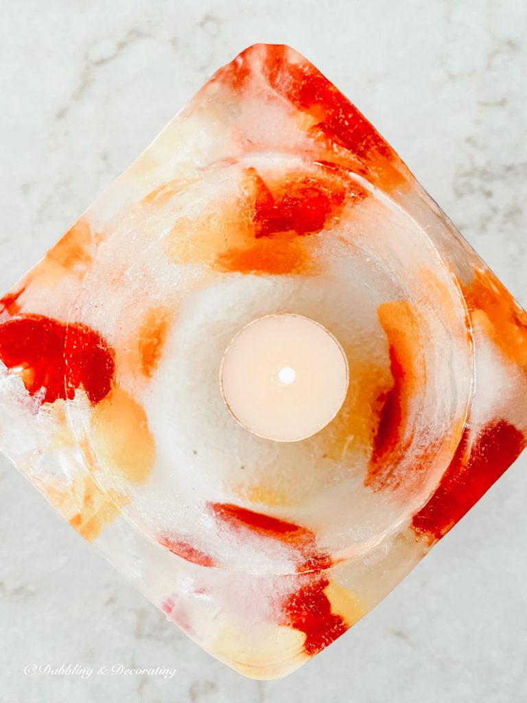 Close up of Ice dandle with red and yellow accents and lit tea light in snow.