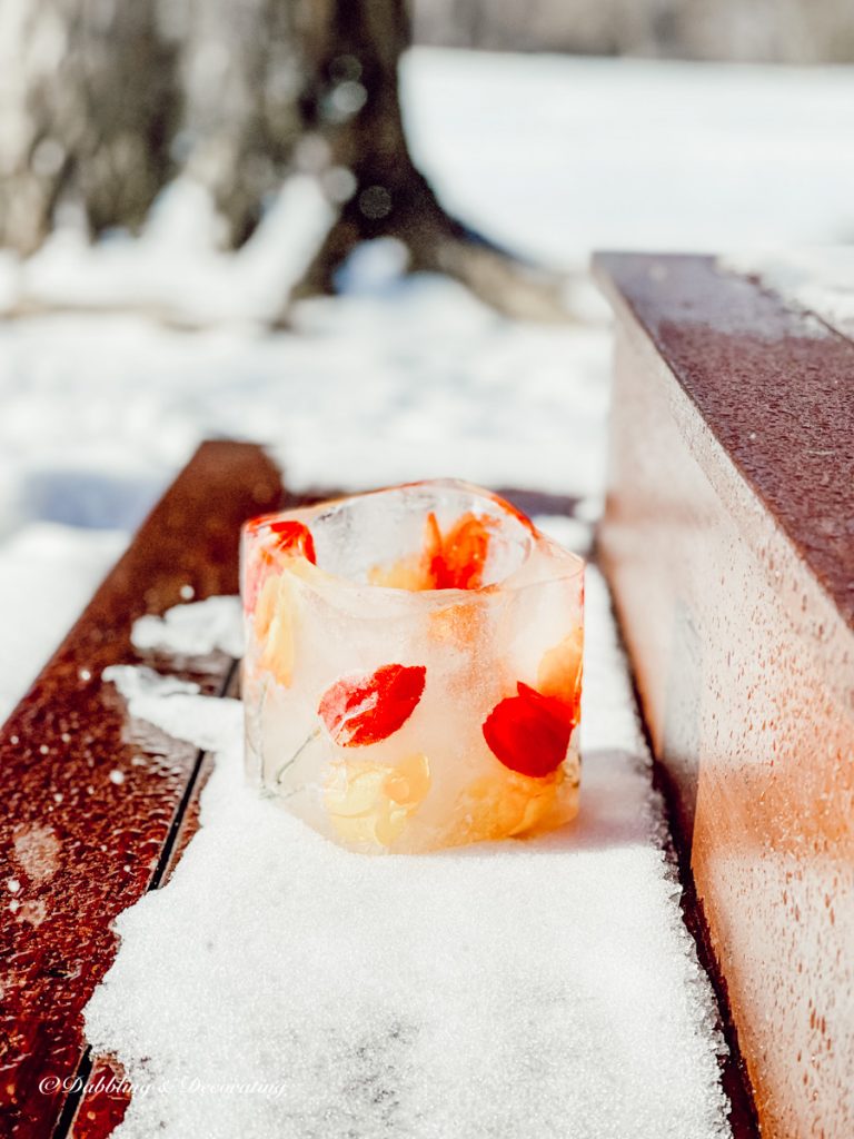 Frozen ice candle sitting in snow on porch steps with red and yellow accents.