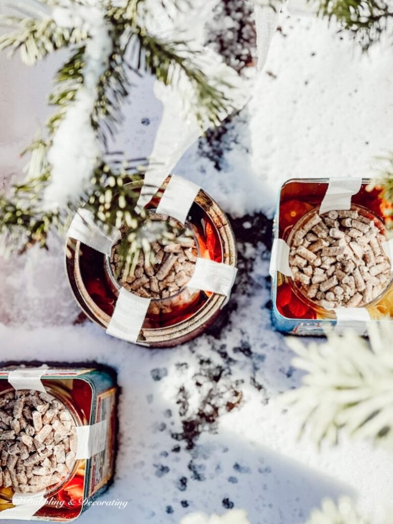 Three tin cans in snow freezing DIY candles for winter diy project.