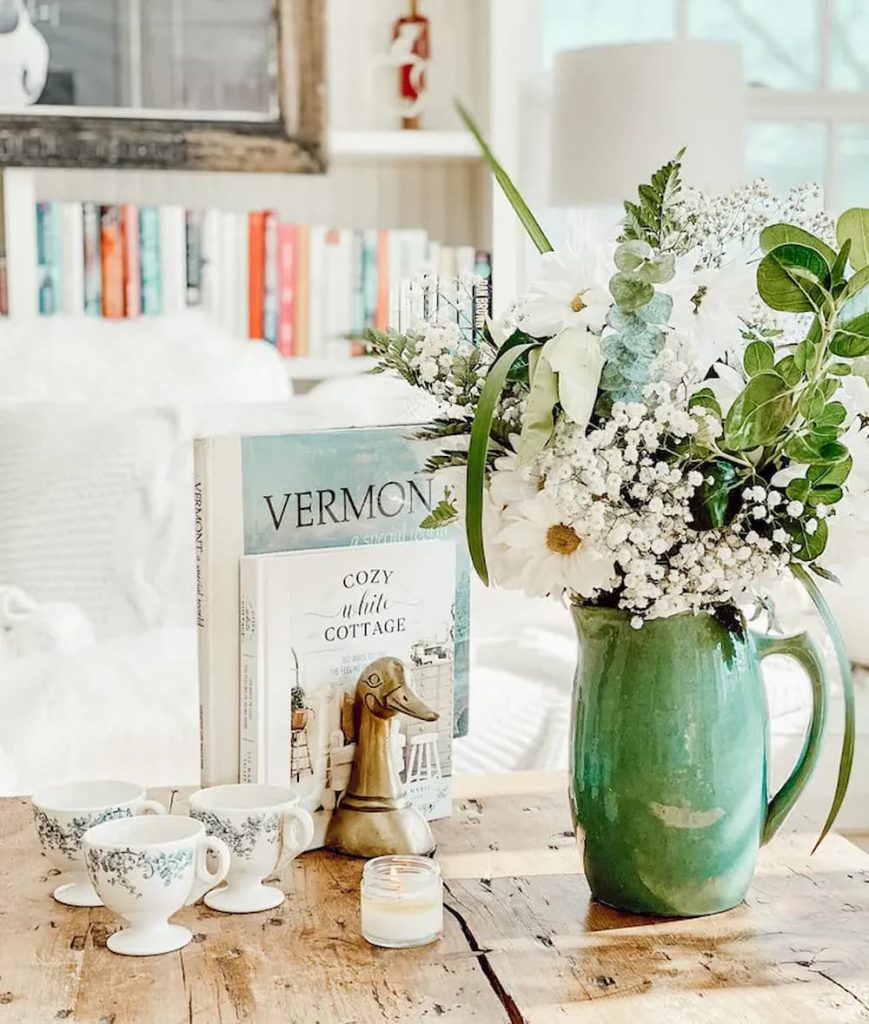 A vintage green vase with flowers and books on a coffee table, perfect for home decor.