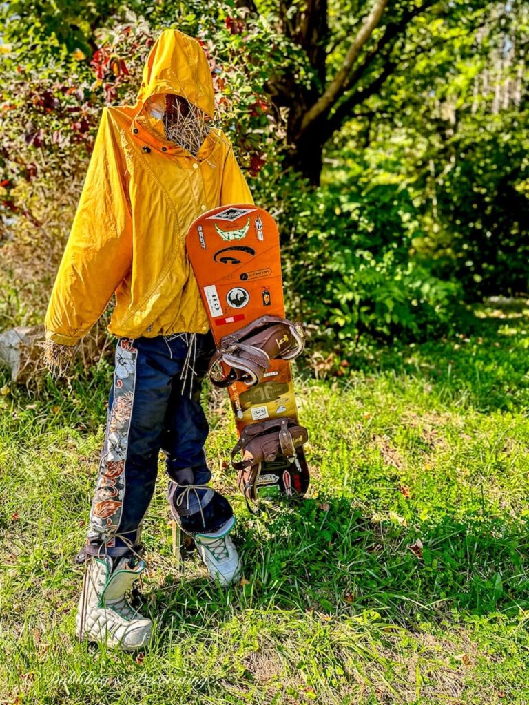 Man scarecrow dressed in orange jacket as snowboarder.