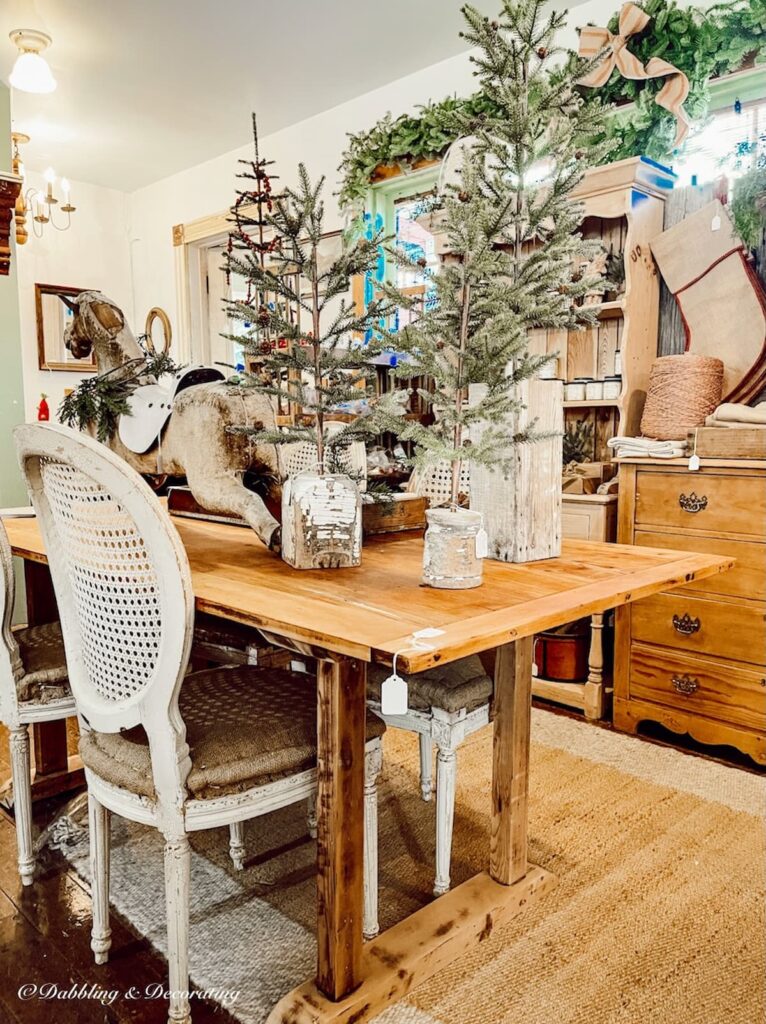 Nordic pine table in antique shop with table top Christmas trees and French chairs.