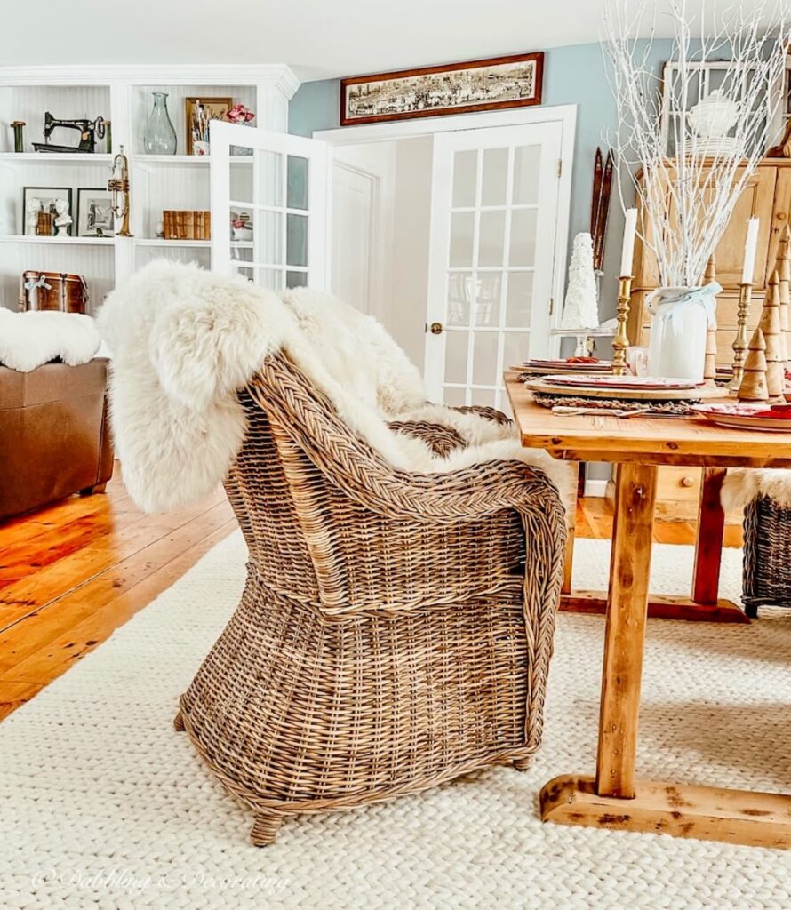 Wicker chairs with sheepskin around a Nordic style on white braided rug in dining room.