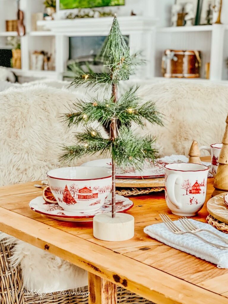 Bico Ceramics Winter Wonderland Toile dinnerware with small Christmas tree on vintage wood table.