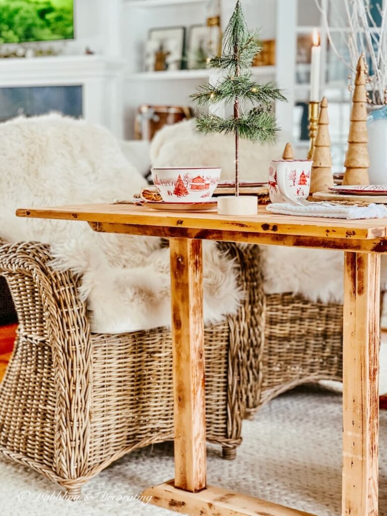 Nordic table with winter wonderland dinnerware, small Christmas tree and sheepskins on wicker chairs close up.