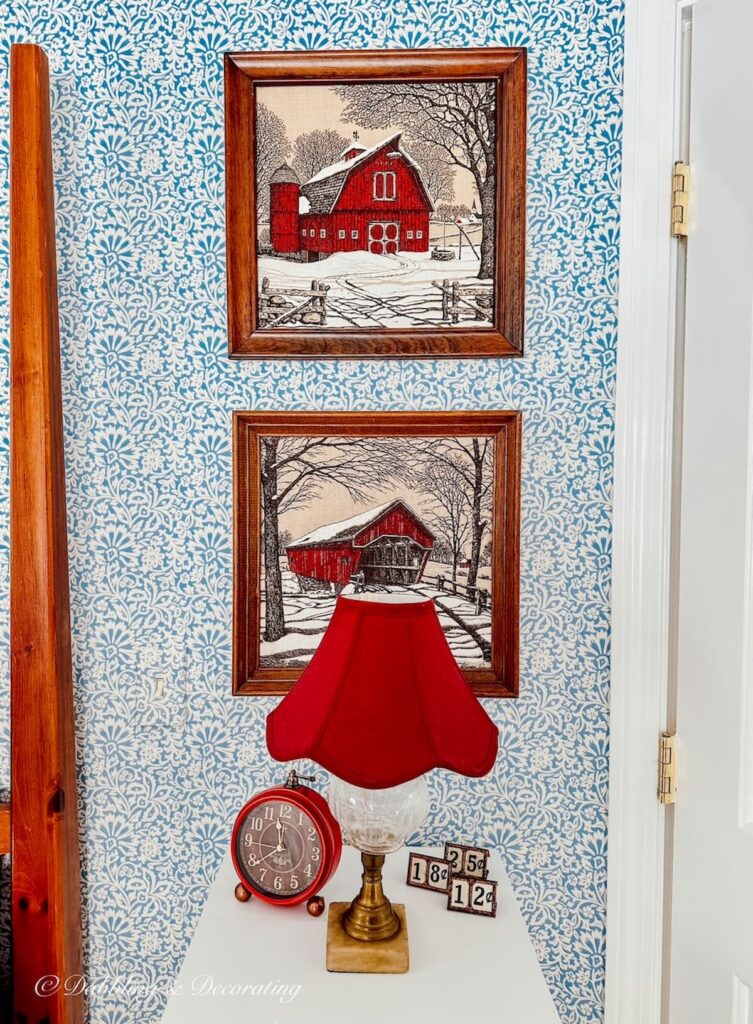 Two Kay Dee prints in wooden frames on bedroom wallpaper blue and white wall over bed side table with red accents.