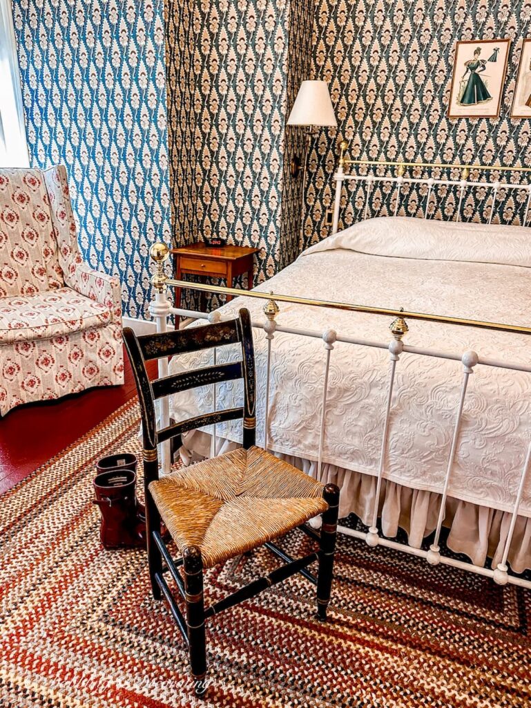 Bedroom wallpaper ideas at the Red Lion Inn in Stockbridge Massachusetts with vintage chair, wrought iron white bed and braided rug.