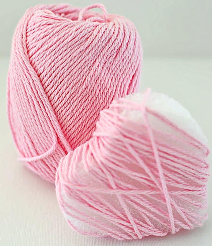 Pink yarn and styrofoam heart being wrapped with the yarn for a DIY heart garland.