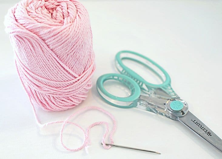 Ball of pink yard with threaded needle and scissors.