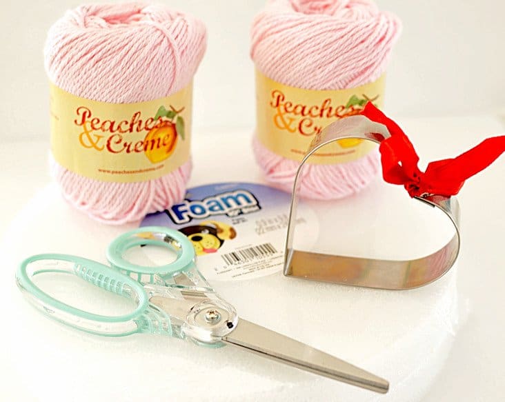 Two balls of pink yarn, scissors, heart cookie cutter and styrofoam, supplies needed for DIY heart garland.