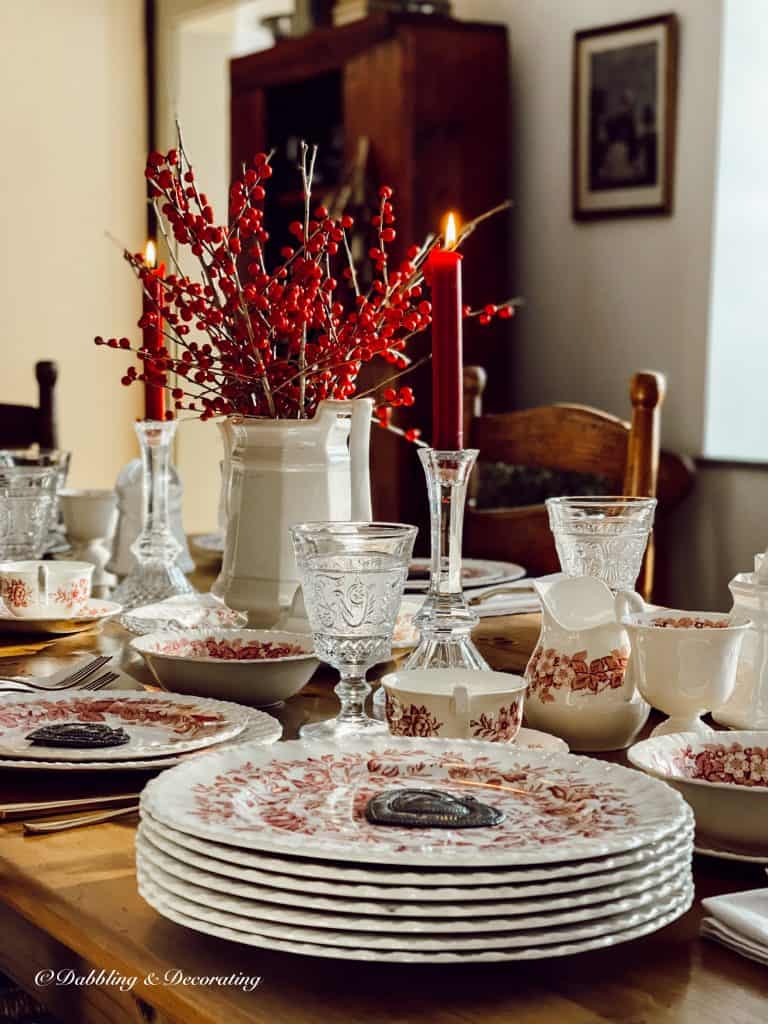 Romantic table setting with winterberry centerpiece and pink and white vintage dishes in antique style dining room.