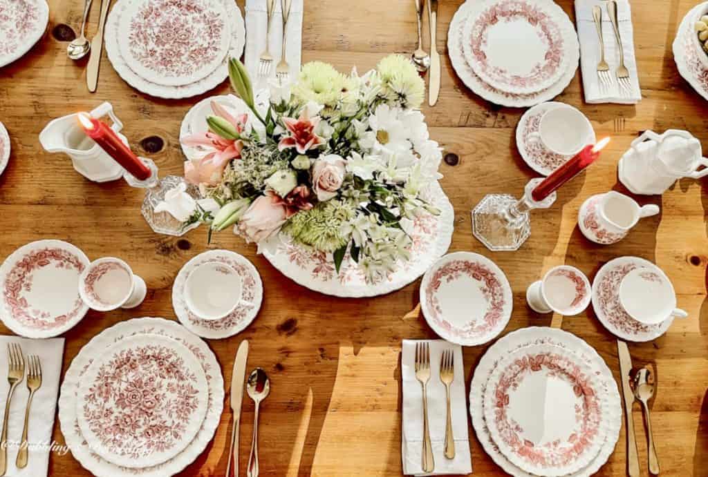 Romantic table setting with pink and white collected vintage dishes and floral arrangement centerpiece.