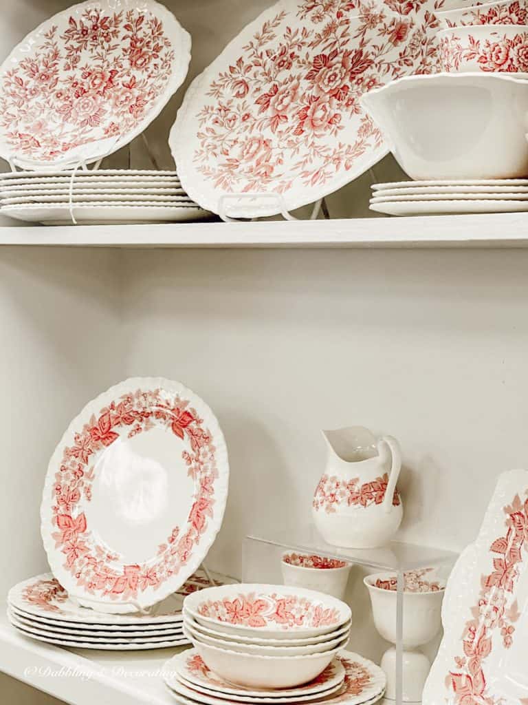 Pink and white vintage dishes displayed on thrift store shelving.