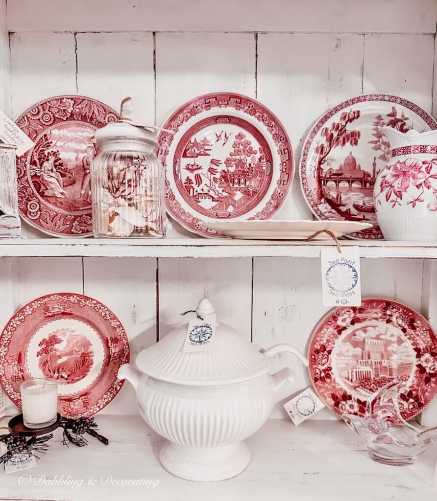 Vintage red and white dishes in a white farmhouse hutch as red decor accents.