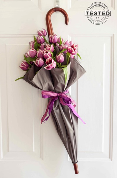 Brown umbrella hanging on white front door with blush tulips and bow.