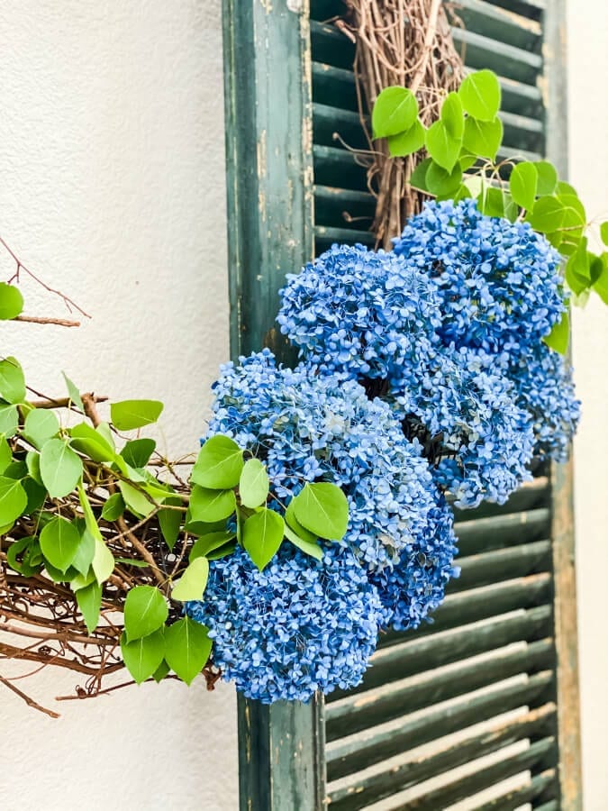 Blue hydrangeas grapevine summer wreath on green shutter.