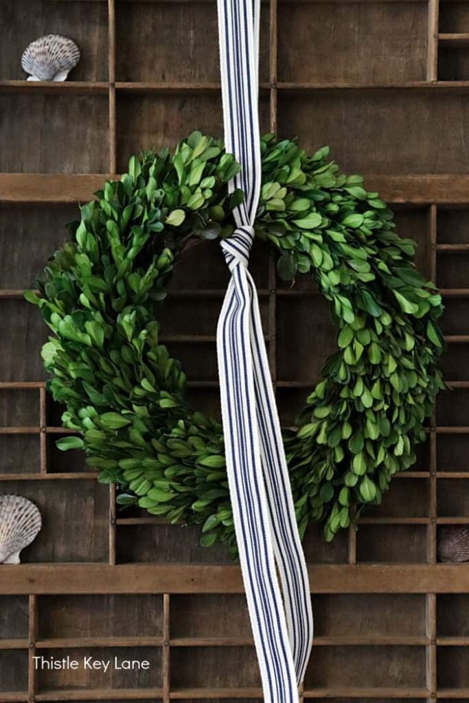 DIY Boxwood wreath with black and white ribbon on vintage printer wooden printer press.