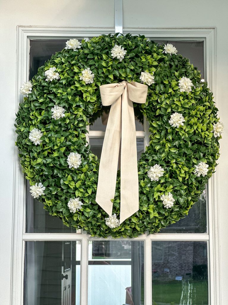 Boxwood Wreath with white flowers and ribbon on front white door.