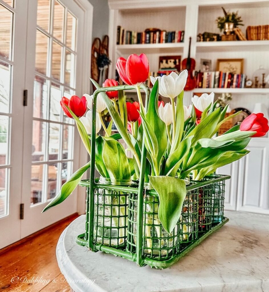 Colorful tulips in green wire garden object on marble table.