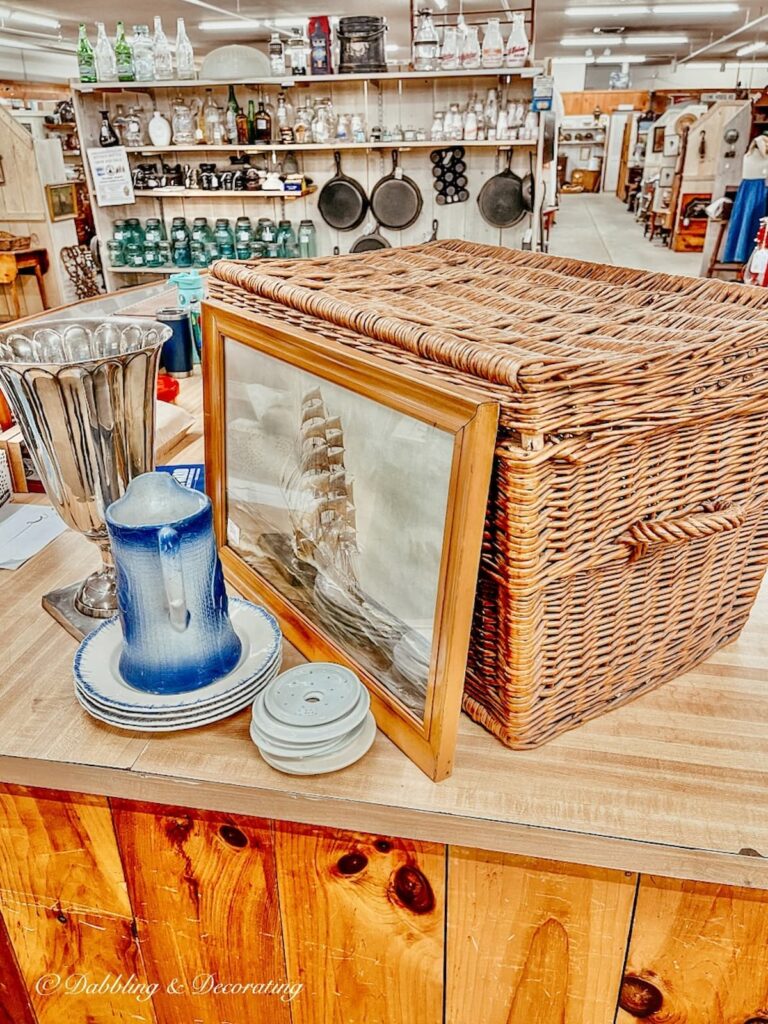 Large basket, painting, blue pitcher on antique shop counter.  A Vintage Haul.