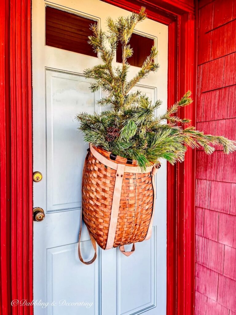 Antique wicker basket backcountry backpack on blue front door with evergreens in home decor.