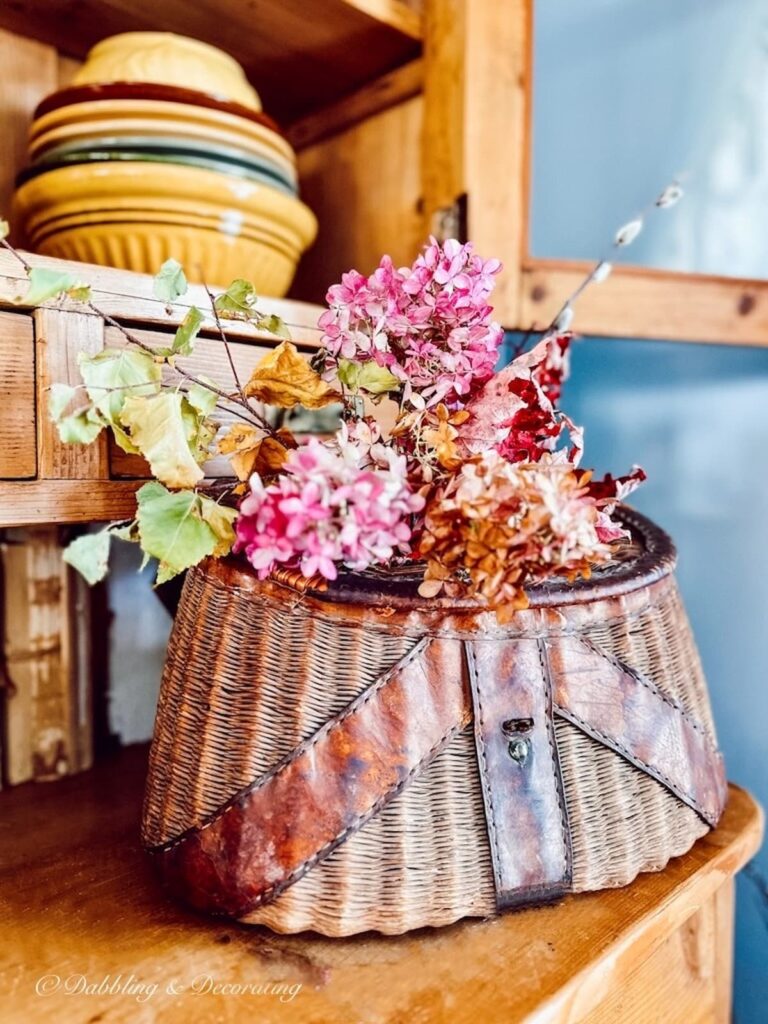 Antique fishing creel basket with dried fall flowers on antique hutch.