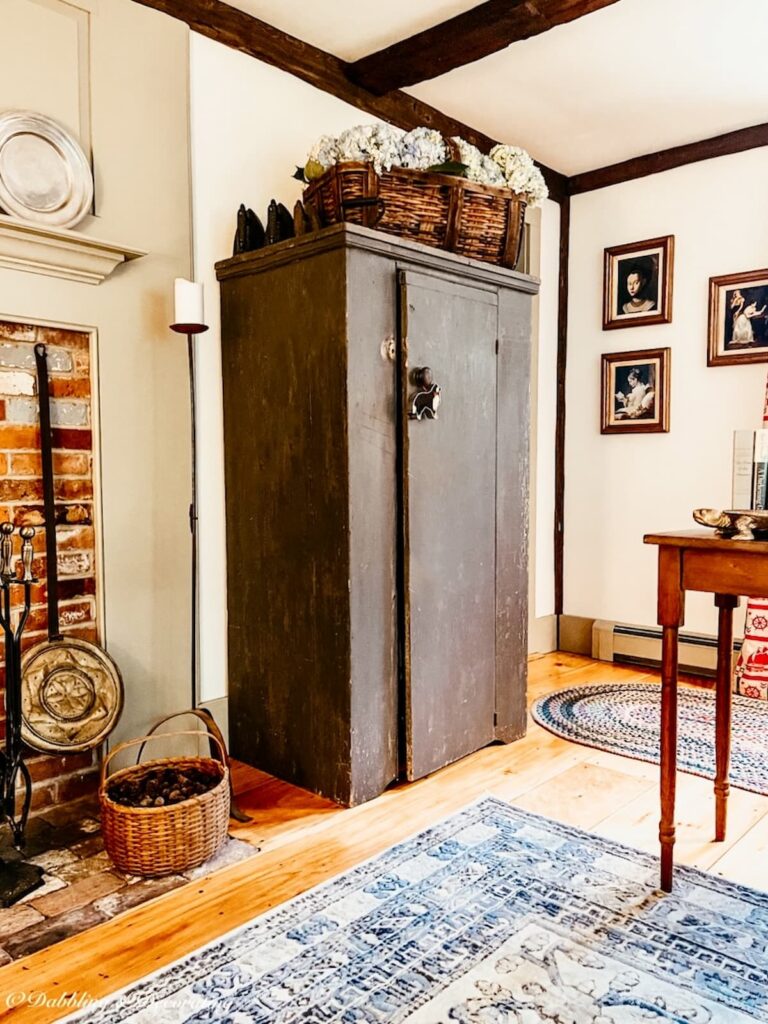 Antique blue hutch with antique basket with blue hydrangeas in living room next to fireplace.