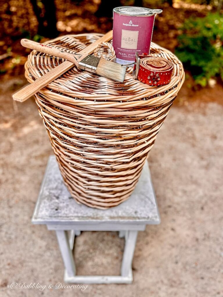 Textured laundry basket with lid and painting supplies and leather belt on white table before.