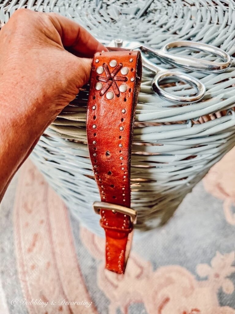 Leather belt in hand aligned with basket DIY and scissors.