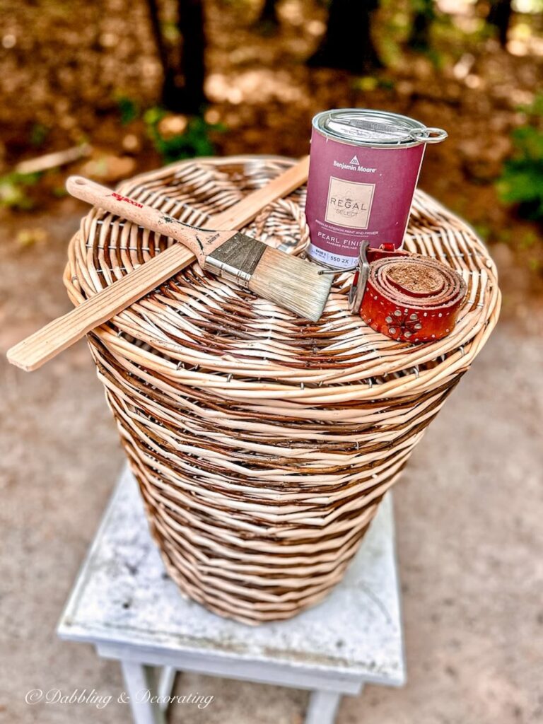 Wicker laundry basket with lid and paint supplies on white table before painting.