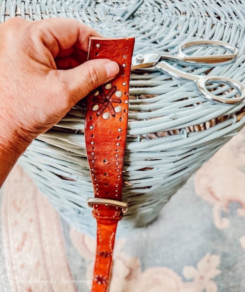 Cut Leather belt in hand aligned with basket DIY and scissors.