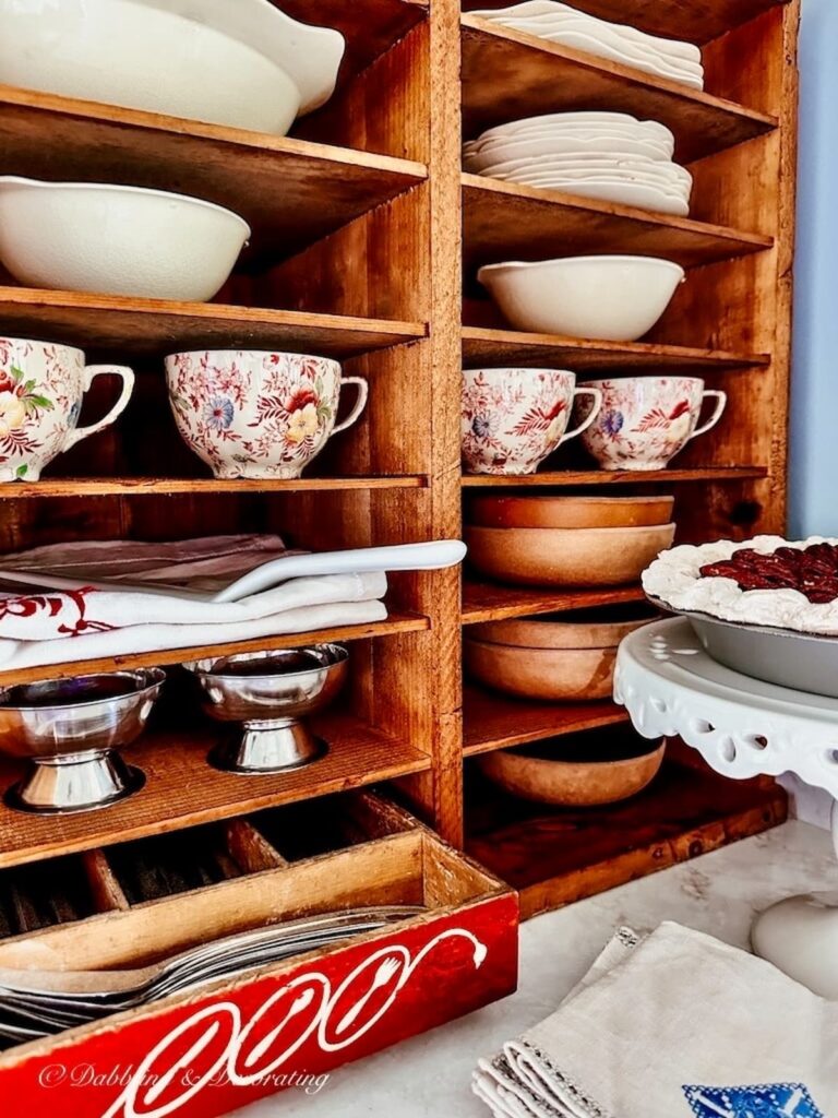 Wooden Pie safe filled with vintage dinner sets and table essentials in kitchen corner.