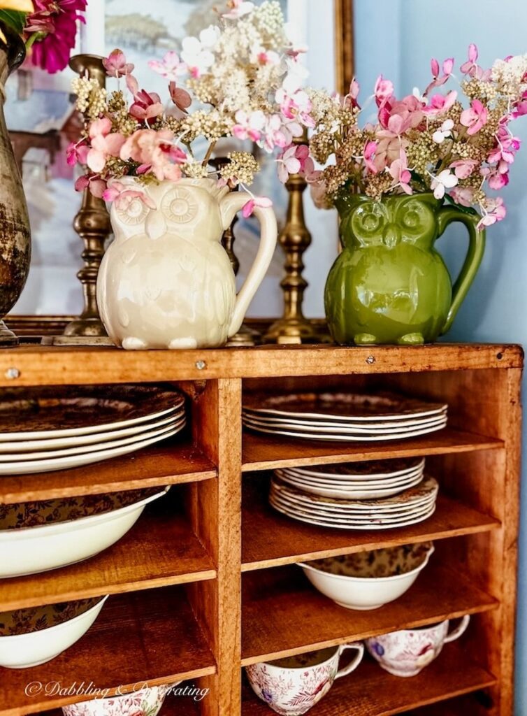 White and Green owl pitchers with pink flowers on top of vintage pie safe in kitchen corner.