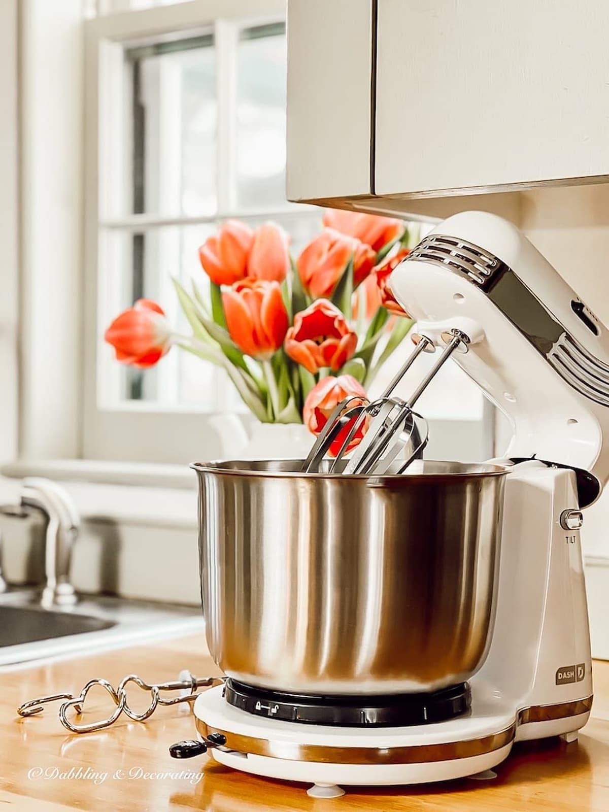 White baking mixer on wooden kitchen counter with pink tulips.