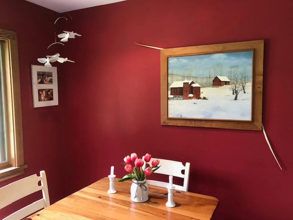 Red Wall Dining Room with red flowers and Vermont snowy painting.