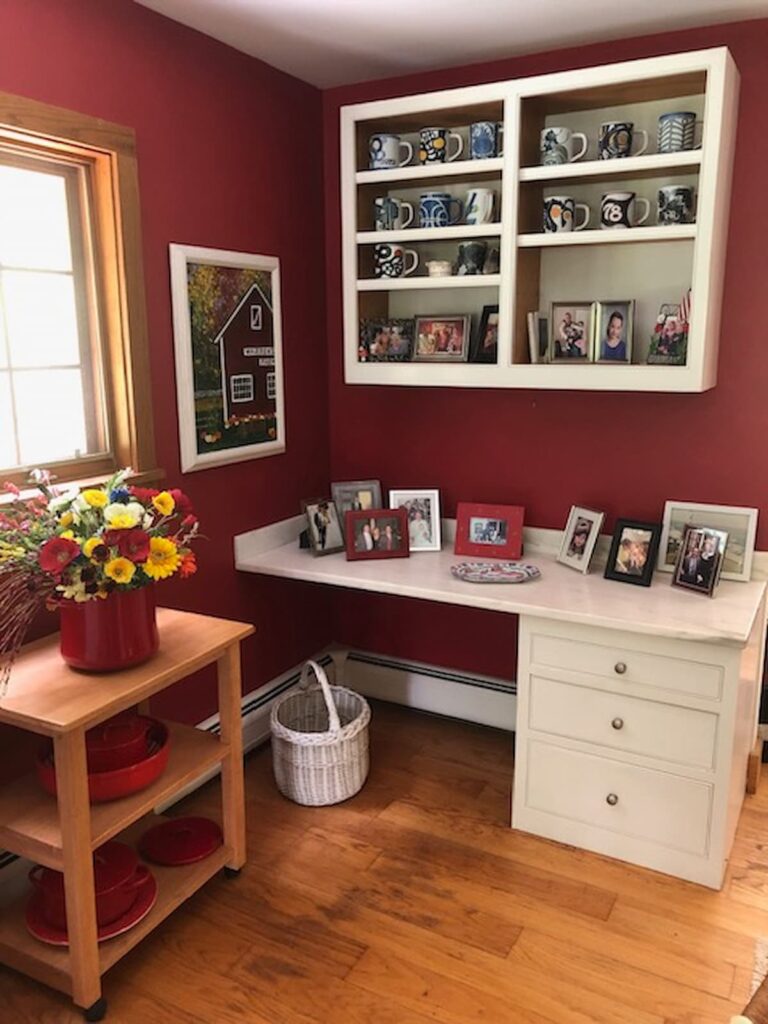 Red wall home office with white desk and shelving and red basket of flowers.
