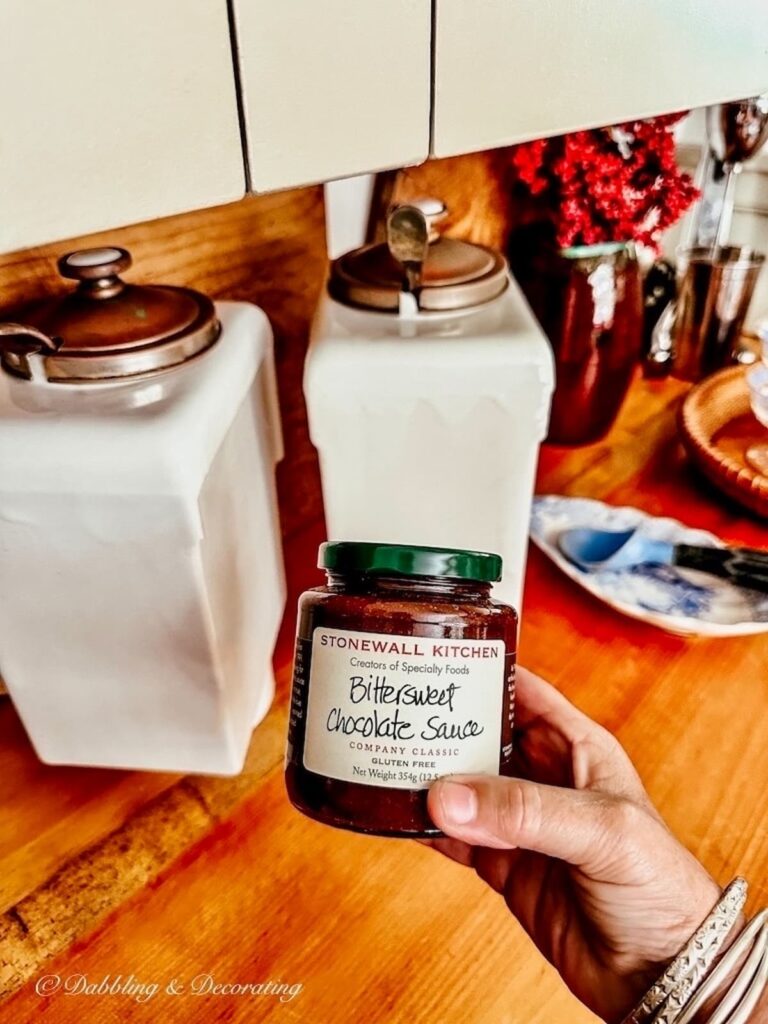 Stonewall Kitchen's Chocolate Sauce in hand next to vintage ironstone ice cream sauce dispensers in country kitchen.