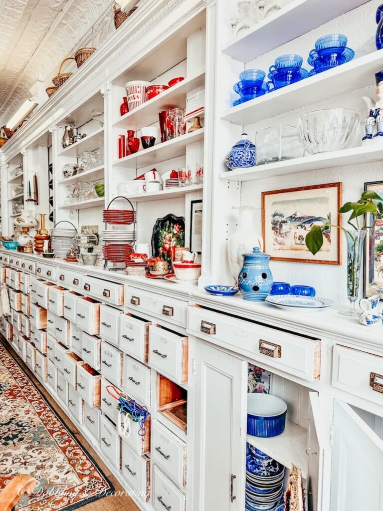 White wall built in shelving and drawers in second chance thrift shop filled with vintage home decor.