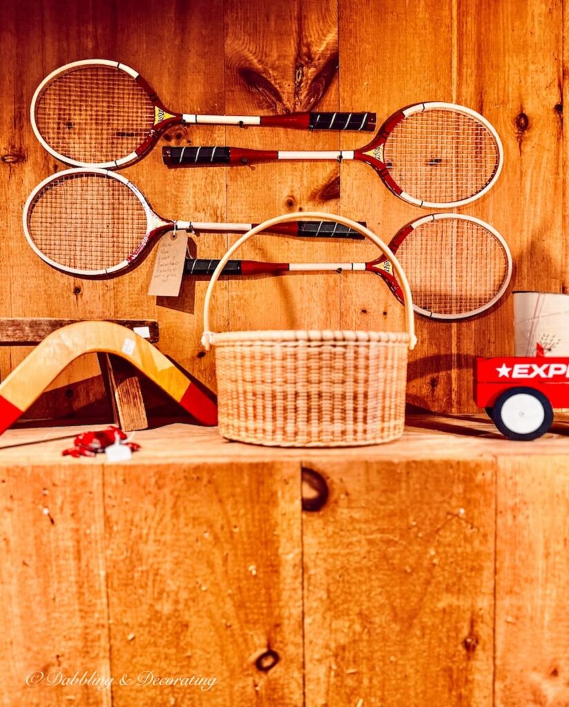 Badminton rackets on wall with boomerang, Nantucket Basket and red truck on shelf at Sage Farm Antiques.