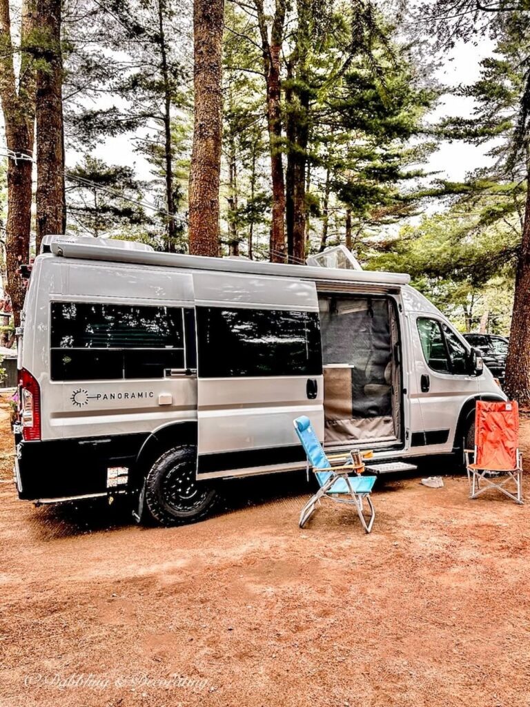 White Panoramic RV at campsite with blue and orange chair next to it.