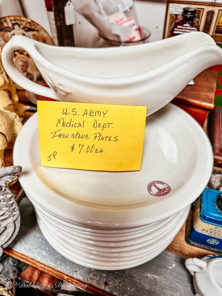 Vintage white dishes and gravy boat with military cafeteria stamp in antique shop.