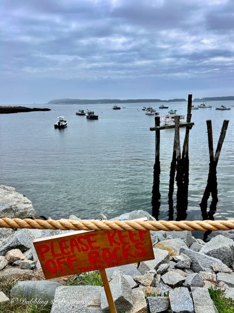 Coastal Maine inlet with boats and warf at McLoon's Lobster Shack and sign that says stay off the rocks.