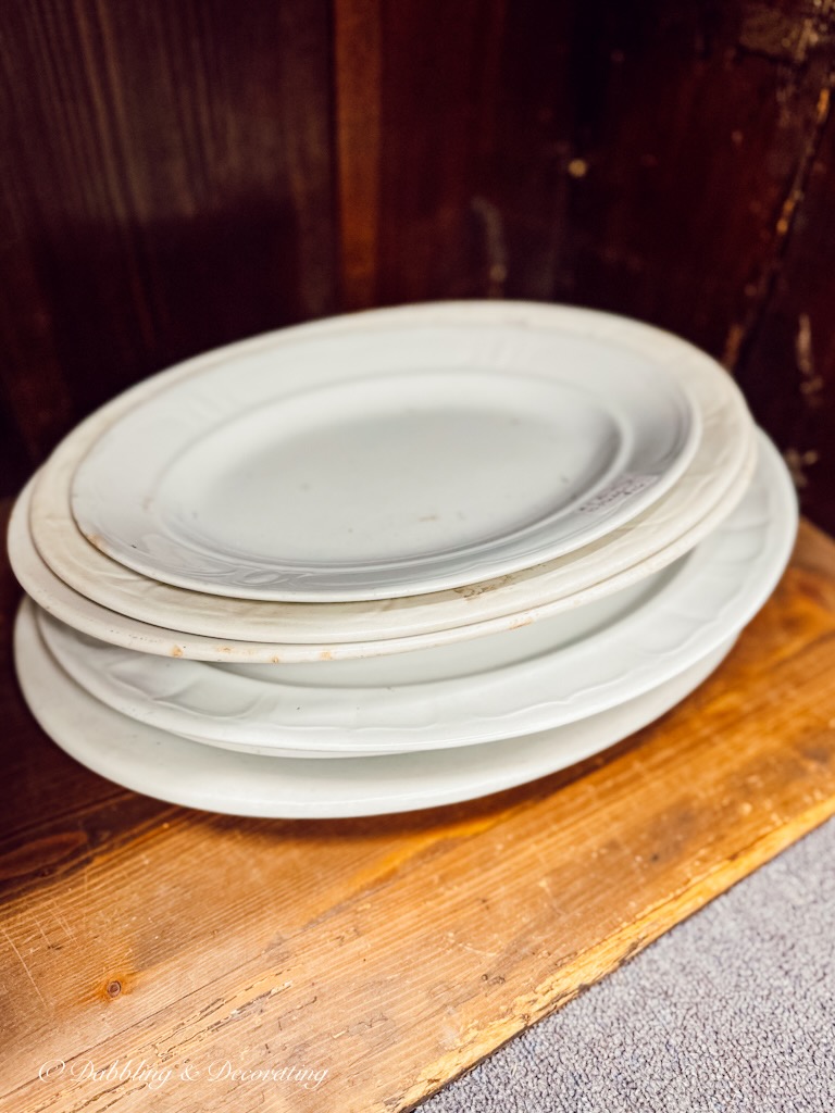 Stack of vintage white ironstone plates in antique shop.