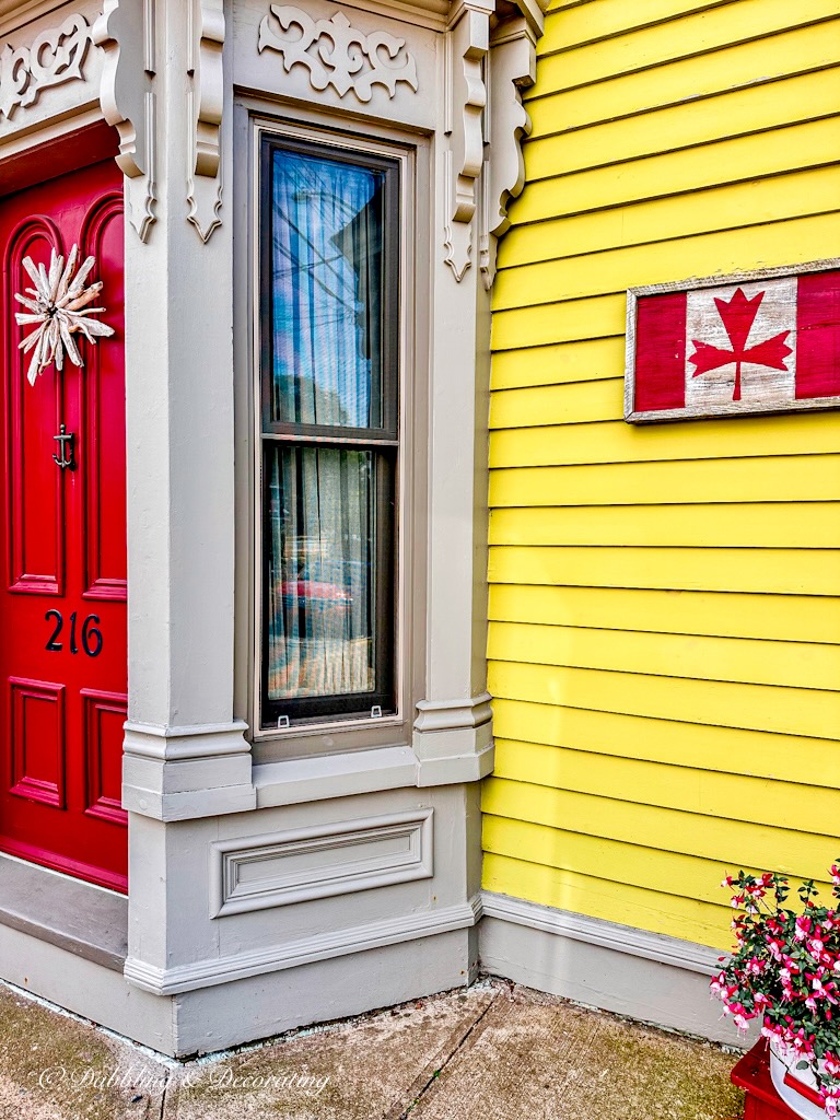 Red Door with Canadian wooden flag on yellow outdoor home exterior on Nova Scotia Road Trip.