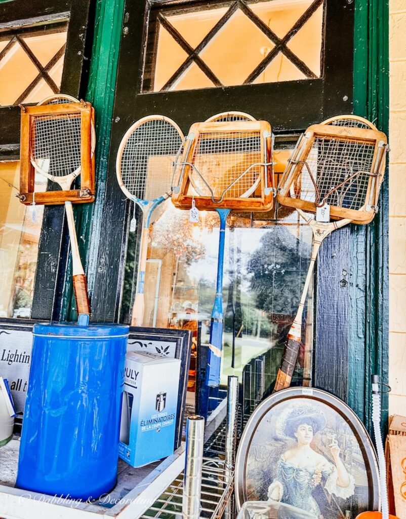 Four vintage badminton rackets with old presses hanging on porch wall at antique shop.