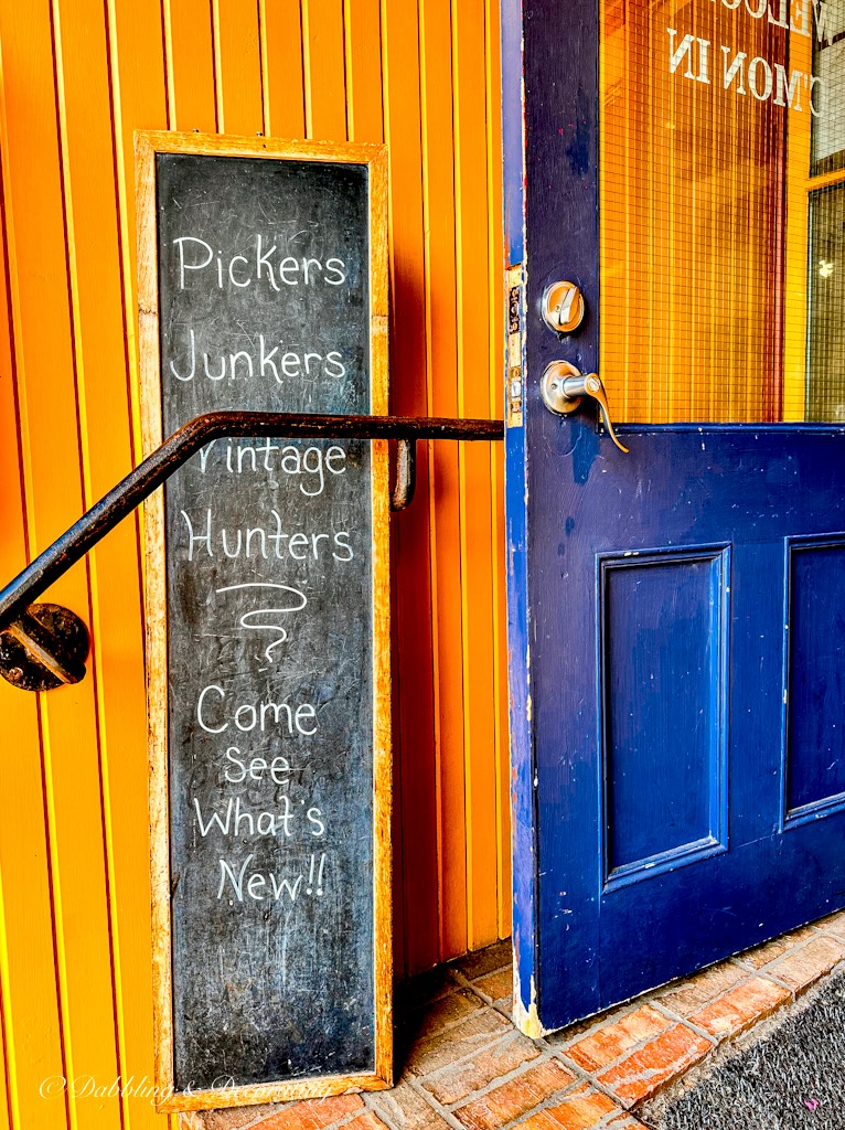 Blue shop door with chalkboard sign that says Pickers, Junkers, Hunters, Come See What's New.